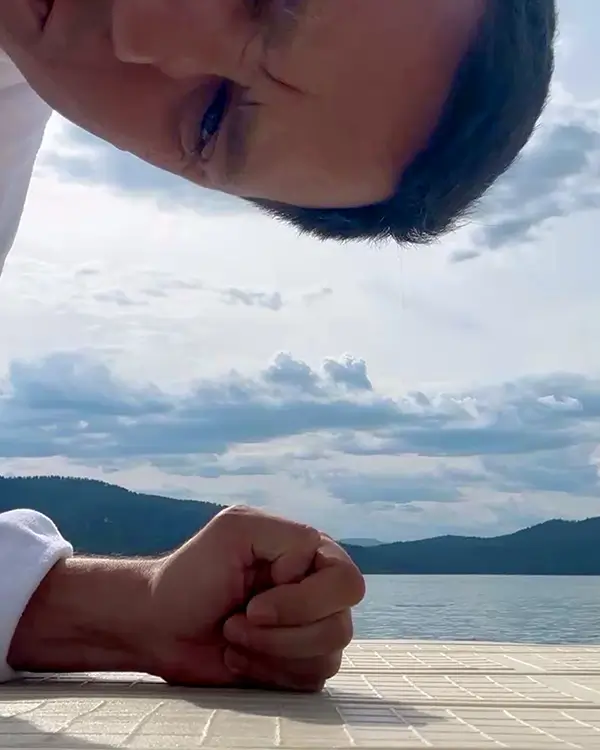 person leaning into the camera with mountains and water in the background