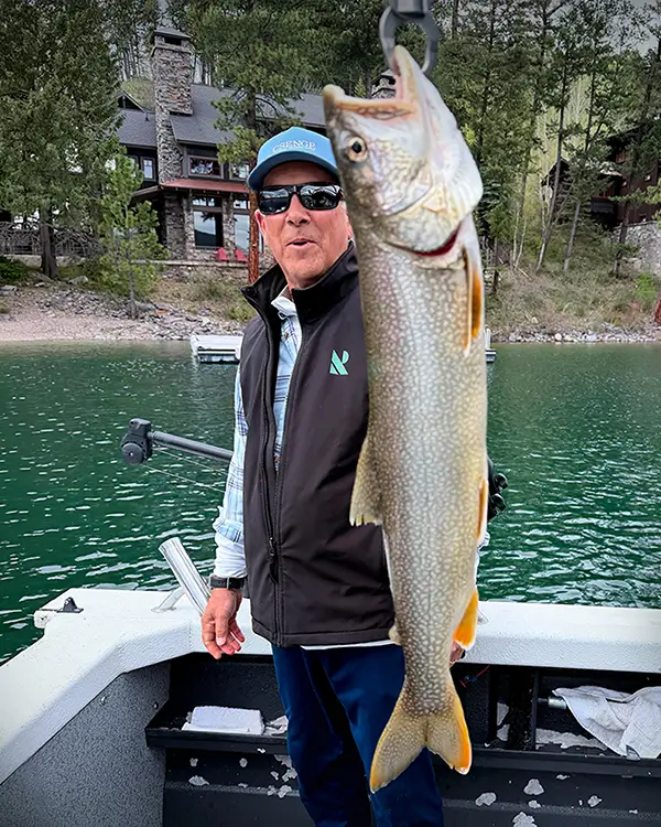 man holding a large fish beside a mountain lake