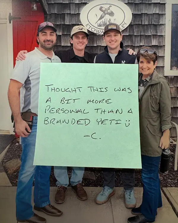 four people standing together holding a framed handwritten note